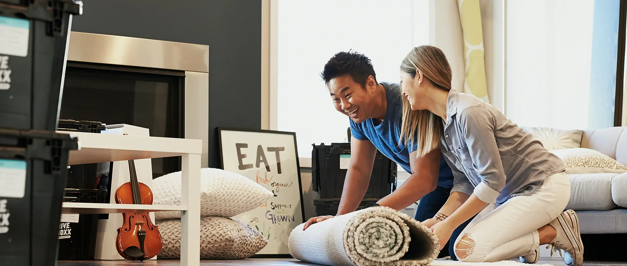 A couple laughing as they unroll a rug in their new home