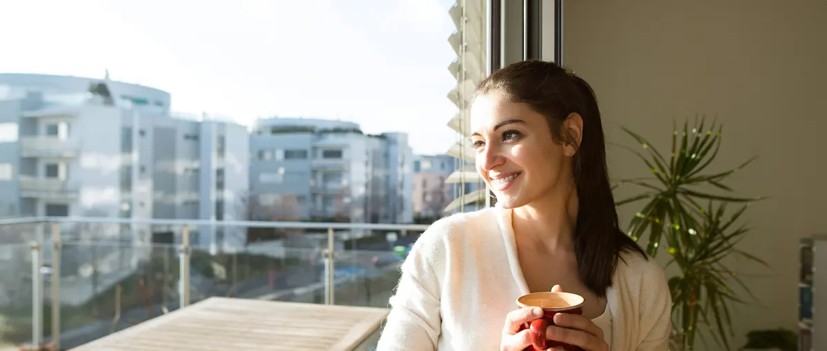 A woman with a mug smiling on her balcony