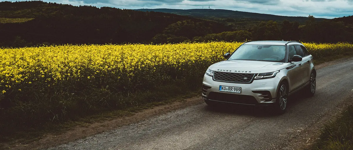 An SUV driving along a country road past yellow fields